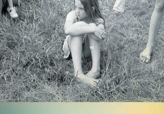 A girl sitting in the grass with her arms crossed.